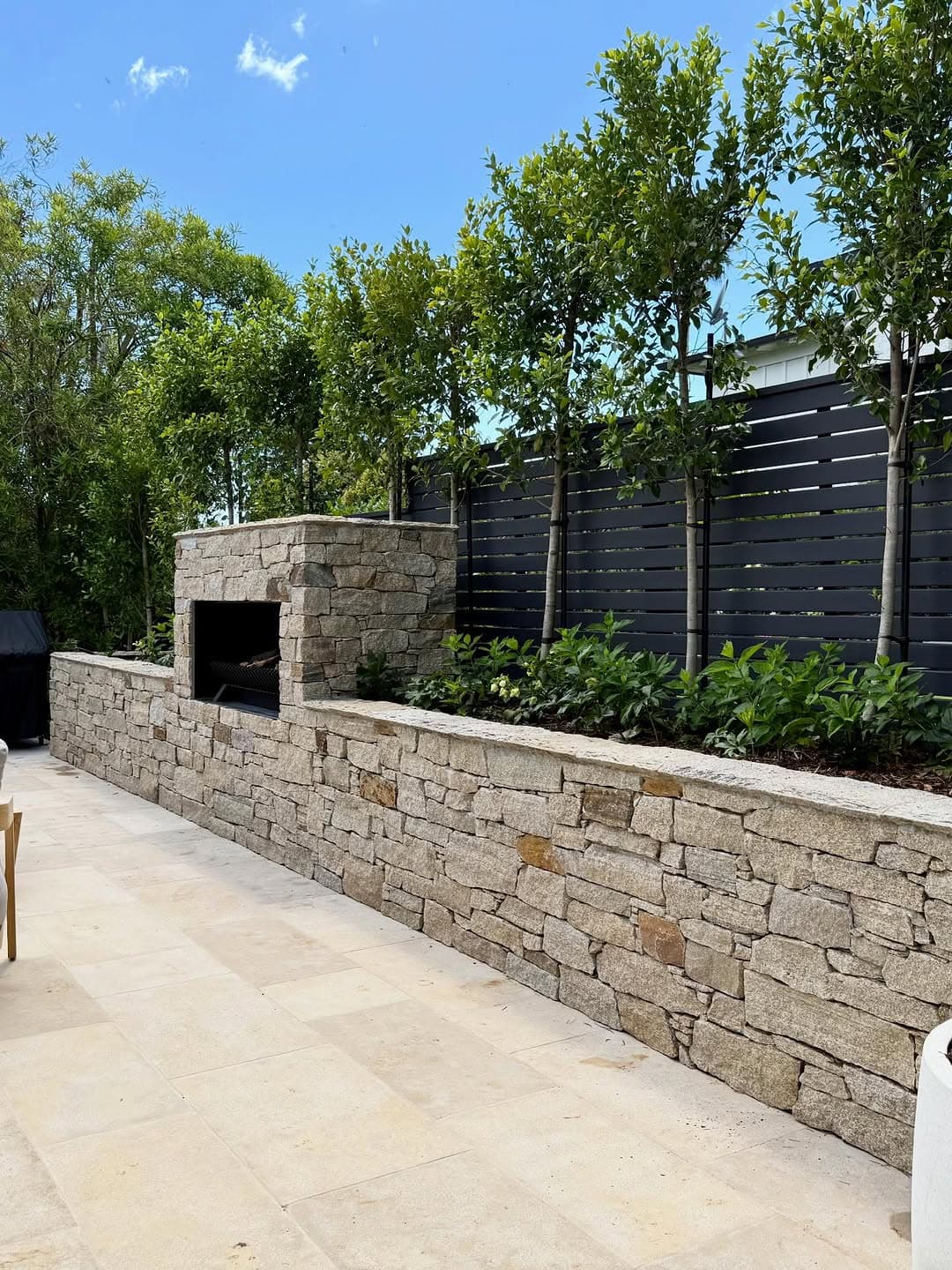 Travertine paving beside stone wall and outdoor fireplace